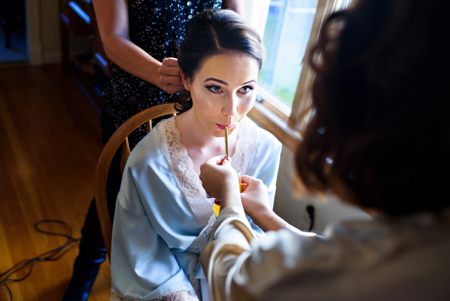 A maid of honor helps the bride hydrate while she gets her hair done before the wedding.